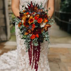 a woman in a wedding dress holding a bridal bouquet with red and orange flowers