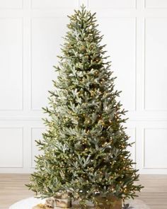 a small christmas tree with lights and presents on the floor in front of a white wall