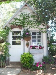 a small white house with flowers growing on the front door and window boxes above it