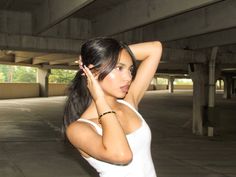 a woman with her hand on her head in an empty parking garage area, wearing a white tank top