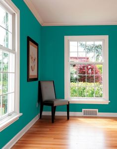 an empty room with blue walls and wood flooring in the center, there is a chair next to a window