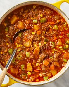 a pot filled with stew and vegetables on top of a white countertop next to a wooden spoon