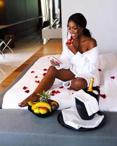 a woman sitting on top of a bed holding a cell phone and fruit in front of her