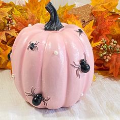 a pink pumpkin with black eyes and spider legs painted on it, next to fall leaves