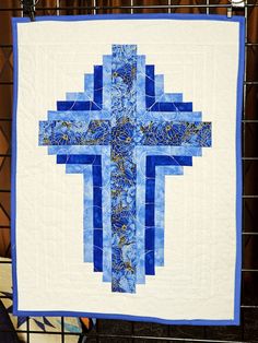 a blue and white quilt with a cross on it's side hanging from a wire rack