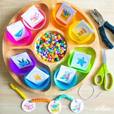 a wooden tray filled with lots of crafting supplies next to scissors and paper plates