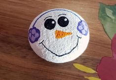 a painted rock with a snowman's face sitting on a wooden table next to flowers