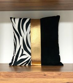 two black and gold pillows sitting on top of a wooden shelf