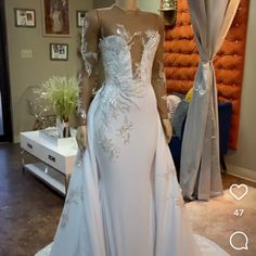 a white wedding dress with sheer sleeves and beading on the boudre is displayed in front of a mirror