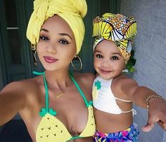 a woman in a yellow bathing suit holding a baby wearing a yellow head wrap and smiling at the camera