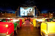 an empty movie theater with rows of chairs and tables in front of a screen on the wall