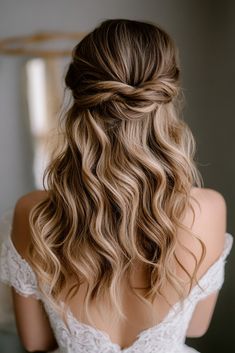 the back of a woman's head with long wavy hair in half updo