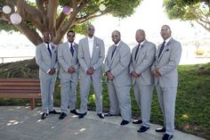 a group of men in suits standing next to each other on a brick walkway under a tree