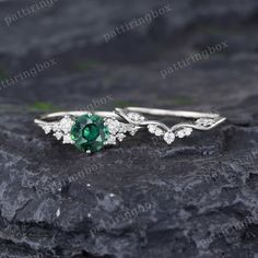 an emerald and diamond ring sitting on top of a rock