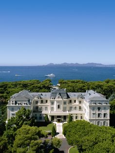 an aerial view of a large white house surrounded by greenery and blue ocean in the background