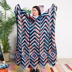 a woman holding up a colorful blanket on top of a rug next to a potted plant