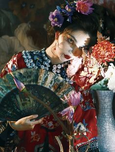 a geisha with flowers in her hair holding a fan and looking at the camera