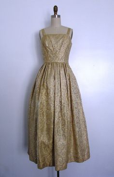 This vintage late 1950s to early 1960s gold damask party dress is gorgeous! This dress is sleeveless, has a square neckline, a cinched waist, the gold damask fabric has a subtle decorative raised floral print, there's a tulle underskirt and a hidden back zipper. Simply feminine and heavenly. A great holiday evening party dress. Effortless and oh so pretty! Pair with a great pair of gold or black shoes and evening bag. Perfect for a formal holiday party. ------------------------------------------ Gold Brocade Dress For Gala, Formal Gold Brocade Dress, Vintage Brocade Party Dress, Gold Dress With Pleated Bodice For Wedding, Gold Wedding Dress With Pleated Bodice, Vintage Fitted Gold Dress, Fitted Vintage Gold Dress, Gold Fitted Vintage Dress, Vintage Ball Gown Dresses For Gala