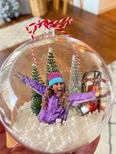 a hand holding a snow globe with a girl in the middle and christmas trees on it