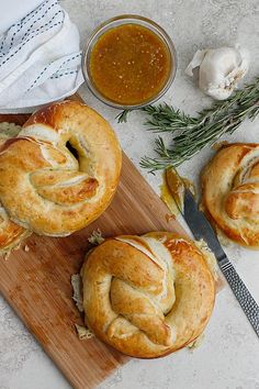 three bread rolls sitting on top of a wooden cutting board next to a bowl of dipping sauce