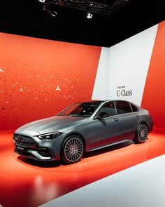 a silver car is on display in front of a red and white wall that says c class