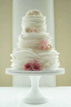 a three tiered wedding cake with pink roses on top and white icing, sitting on a pedestal