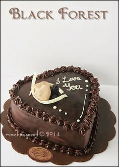 a heart shaped chocolate cake with the words black forest written on it and a small teddy bear