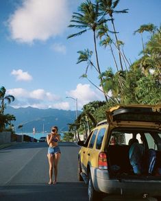 a woman is walking down the street with her luggage in the back of an suv