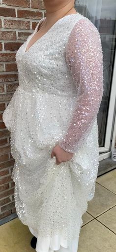 a woman standing in front of a brick wall wearing a white dress with sequins on it