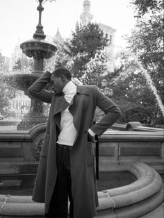 a man standing in front of a fountain with his hands on his head and wearing a coat