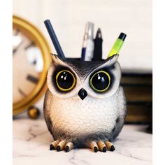 an owl figurine with pens and pencils in it's beak sitting next to a clock