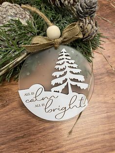 a christmas ornament hanging from a tree on top of a wooden table with pine cones