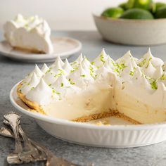 a white plate topped with a cake covered in whipped cream and limes next to a bowl of limes