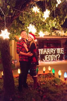 a man and woman standing under a tree with christmas lights