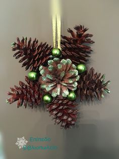 an ornament made out of pine cones and green baubles hangs on a wall