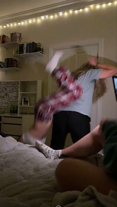 two people playing wii in a bedroom with lights on the ceiling and bookshelves