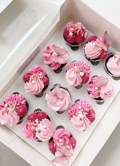 cupcakes with pink frosting and flowers in a white box on a table