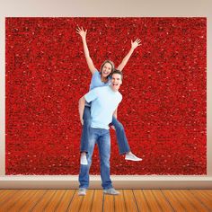 a man and woman are standing in front of a red wall with their arms up