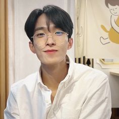 a young man wearing glasses sitting in front of a window