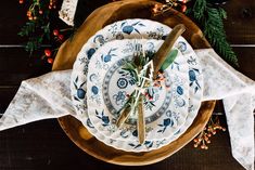 a table setting with plates, napkins and spices on top of each plate is surrounded by greenery