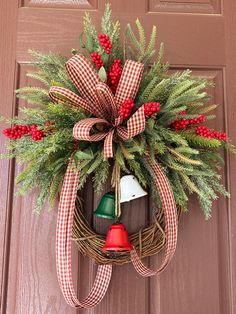 a christmas wreath hanging on a door with a red and white bow, bells and evergreens