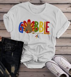 Women's Gobble T Shirt Turkey Shirts Gobble Tee Arrow Feathers Cute Thanksgiving TShirtThis women's gobble t shirt is cute, color, fun, and perfect for Thanksgiving. This colorful thanksgiving tshirt features the word 'Gobble' with a cute winking turkey as the 'o'. Perfect for all family members, commemorate your feast with matching shirts this year! Made of soft ring spun cotton and includes a cotton muslin drawstring gift bag.Direct to garment printed using the latest technology. Soft, ring sp Hipster Graphic Tees, Drawstring Gift Bag, Winter Outfits Aesthetic, Winter Travel Outfit, Casual Shoes Outfit, Mens Fashion Casual Winter