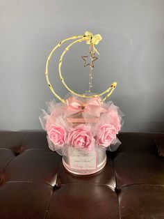 a pink rose arrangement in a round glass container on a brown leather ottoman with a star hanging from the top