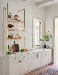 a kitchen with white cabinets and marble counter tops, gold shelving unit on the wall