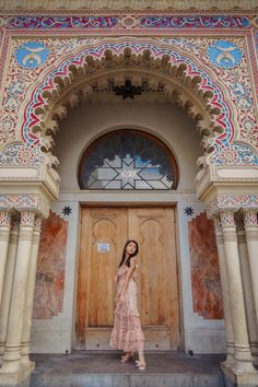 a woman standing in front of a wooden door with ornate designs on the doors and windows