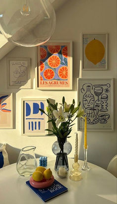 a white table topped with vases filled with flowers and fruit next to pictures on the wall