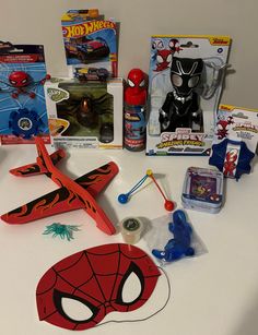 various toys are laid out on a white counter top, including a toy plane and spiderman mask