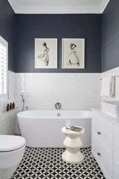 a bathroom with two pictures on the wall above the bathtub and toilet, along with black and white floor tiles