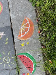 two sidewalk chalk drawings with fruit and stars painted on them, along with grass in the background