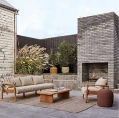 an outdoor living area with couches, tables and chairs in front of a brick wall